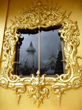 Thaïlande Chiang Rai Temple blanc White Temple De l'or en face du temple blanc que l'on voit en reflet dans la fenêtre de ce curieux palais doré